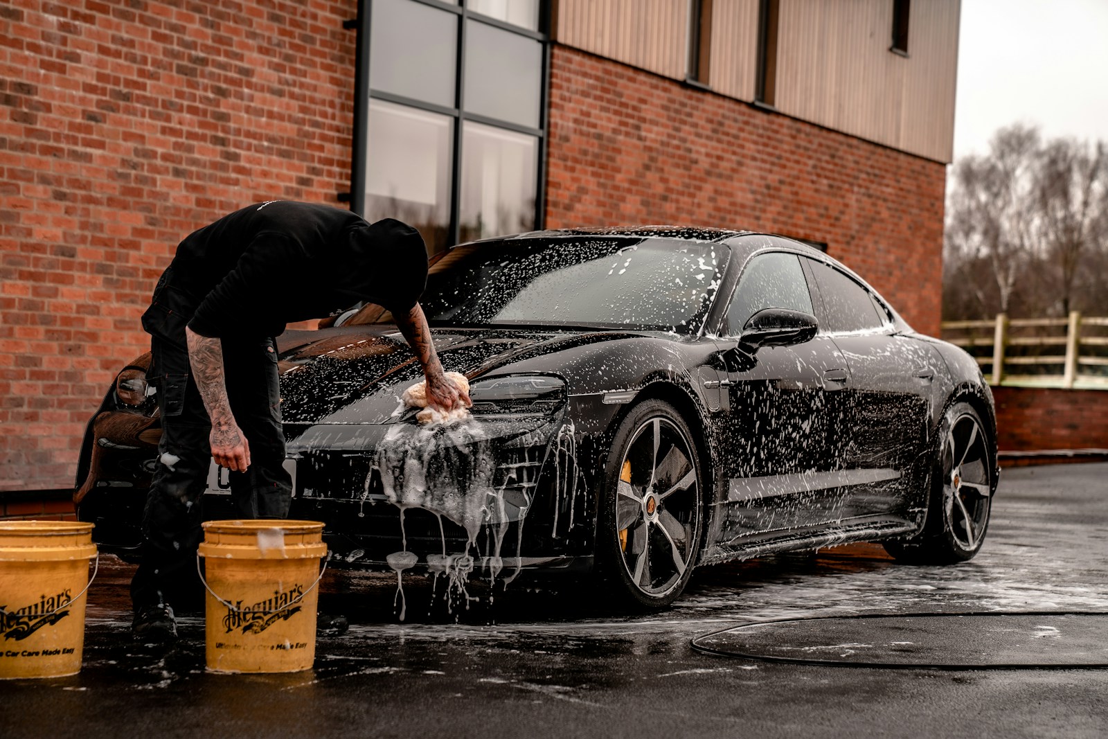 Services man in black t-shirt and black pants doing water splash on black coupe during daytime